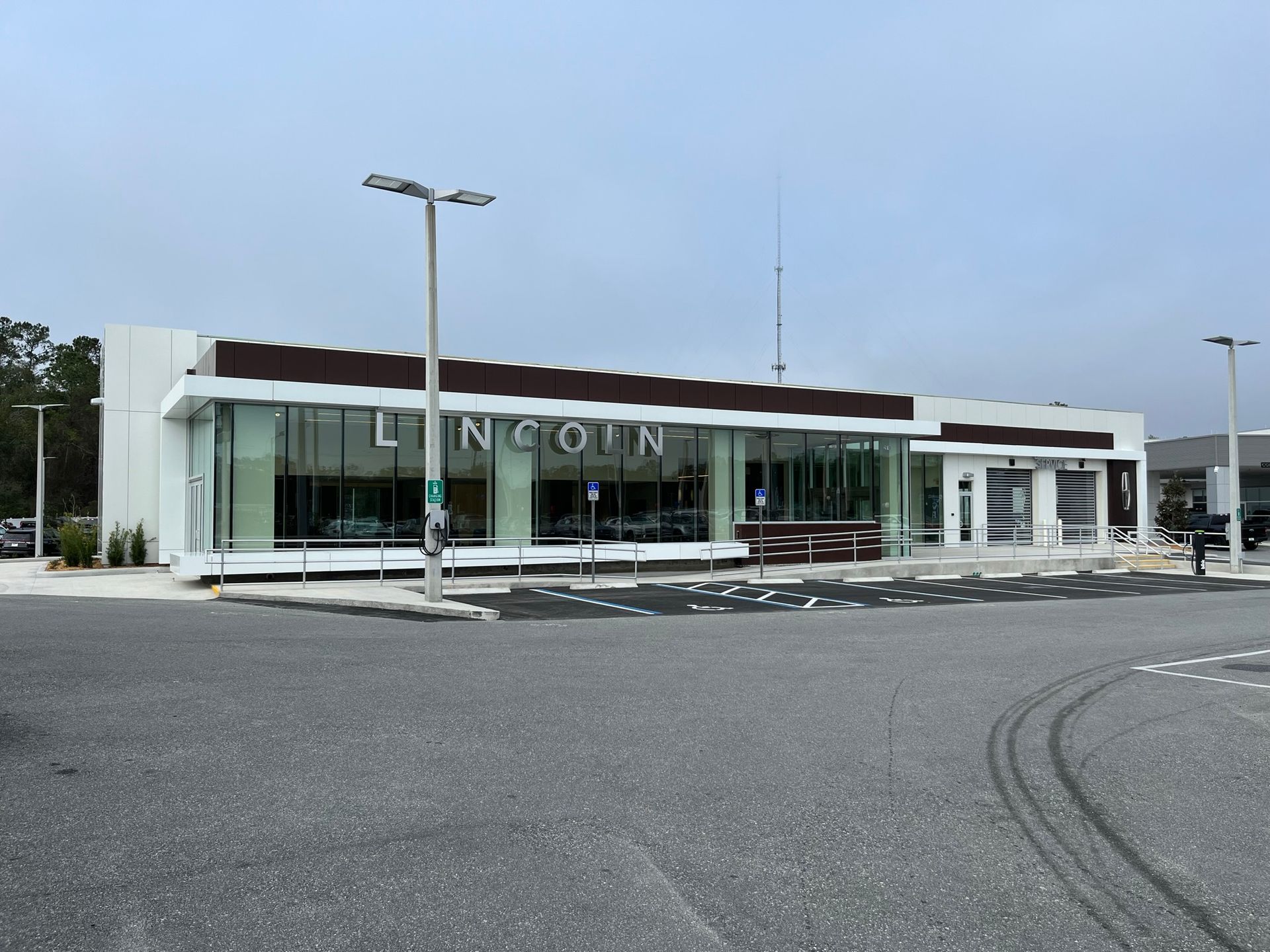 A modern Lincoln car dealership with large glass windows, a white facade, and a dark brown accent roof under a cloudy sky.