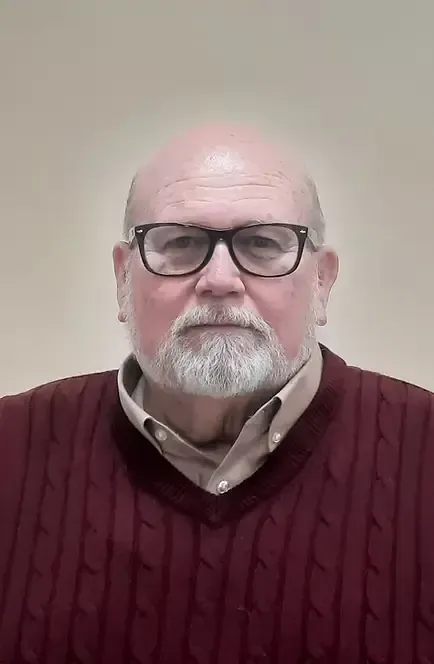 Man with glasses and beard, wearing a burgundy sweater over a light-colored collared shirt, against a beige background.