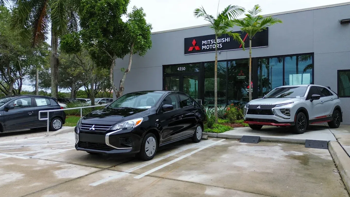 A Mitsubishi dealership building with a black car parked in front and a silver SUV to the side.