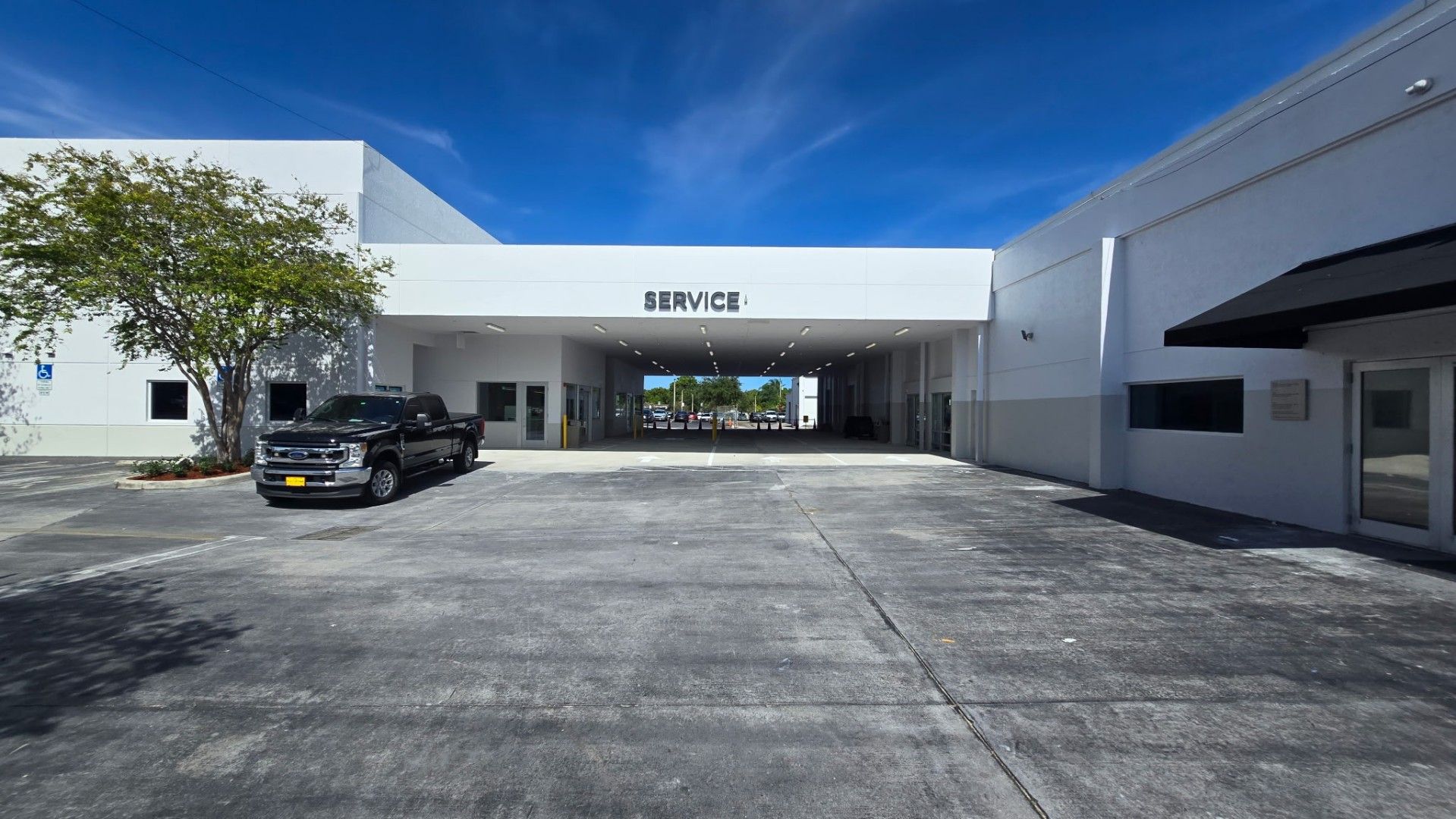 A sunny view of a large white commercial building with a central breezeway and a parked black truck in the foreground.