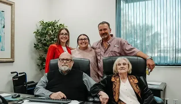 Group of five people posing in an office. Two seated, three standing behind them.