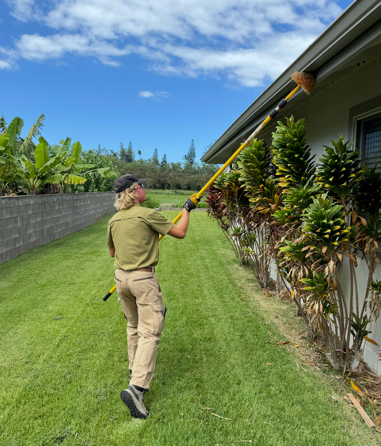 Pest control worker standing by truck, holding sprayer. He wears a cap, khaki pants, and a backpack, near a logo.