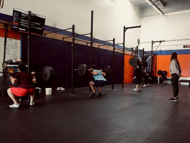 A group of people are squatting with barbells in a gym.