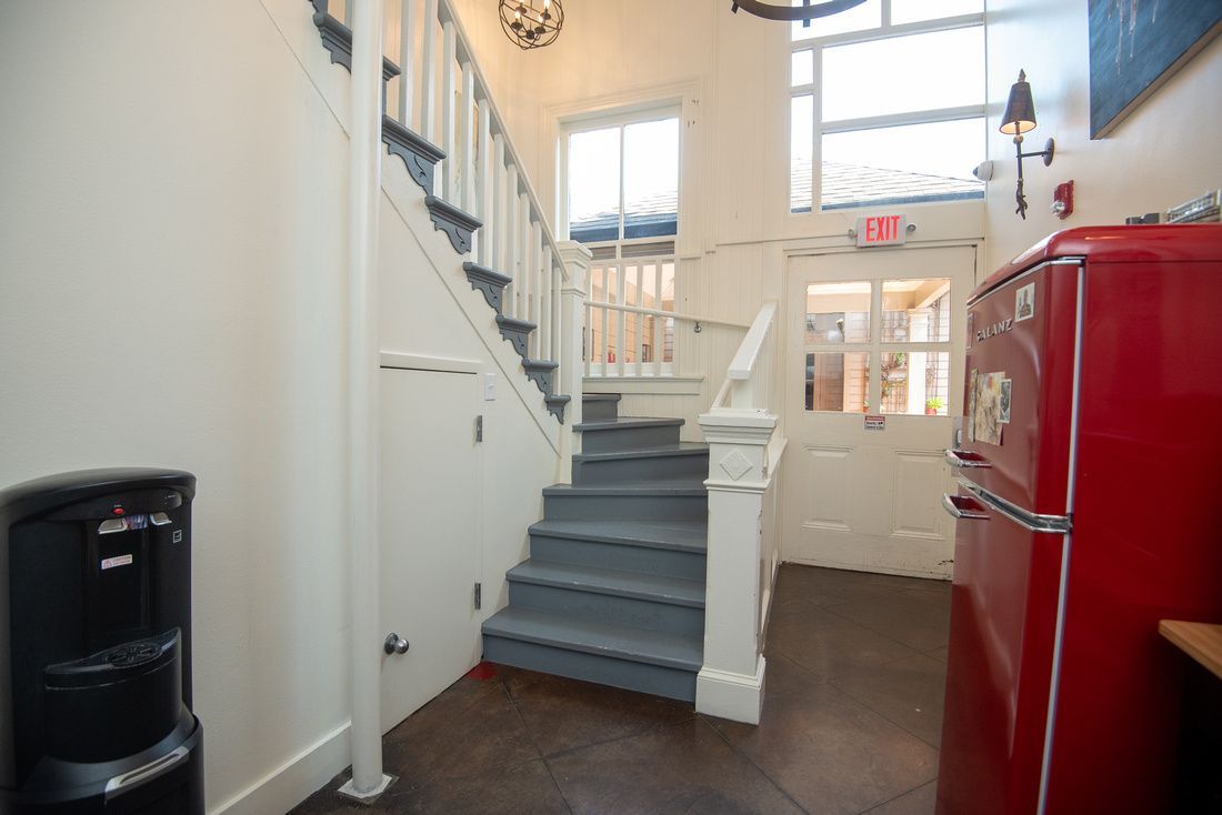 A red refrigerator is next to a staircase in a hallway.