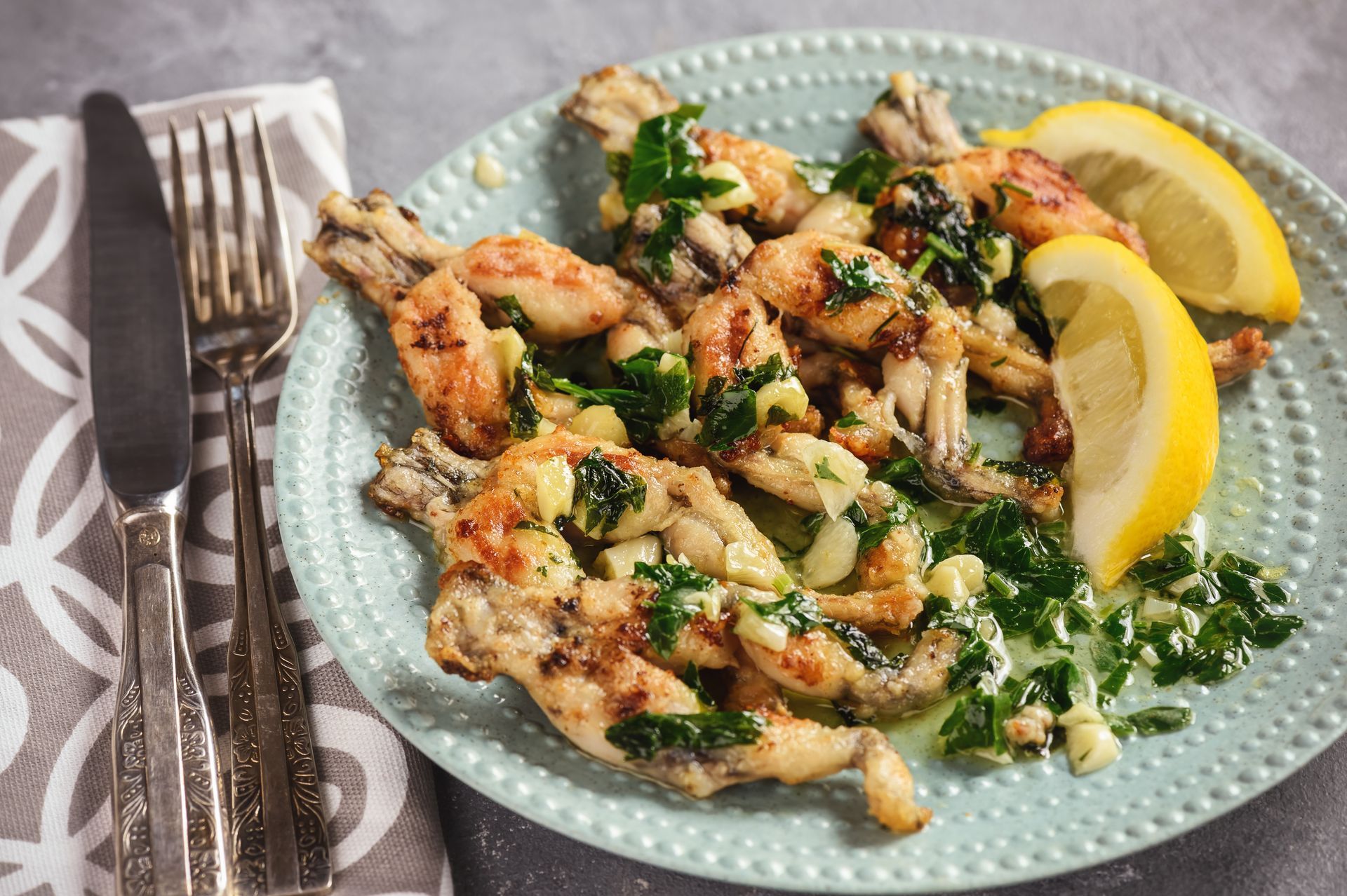 A plate of frog legs with lemon slices and parsley on a table.