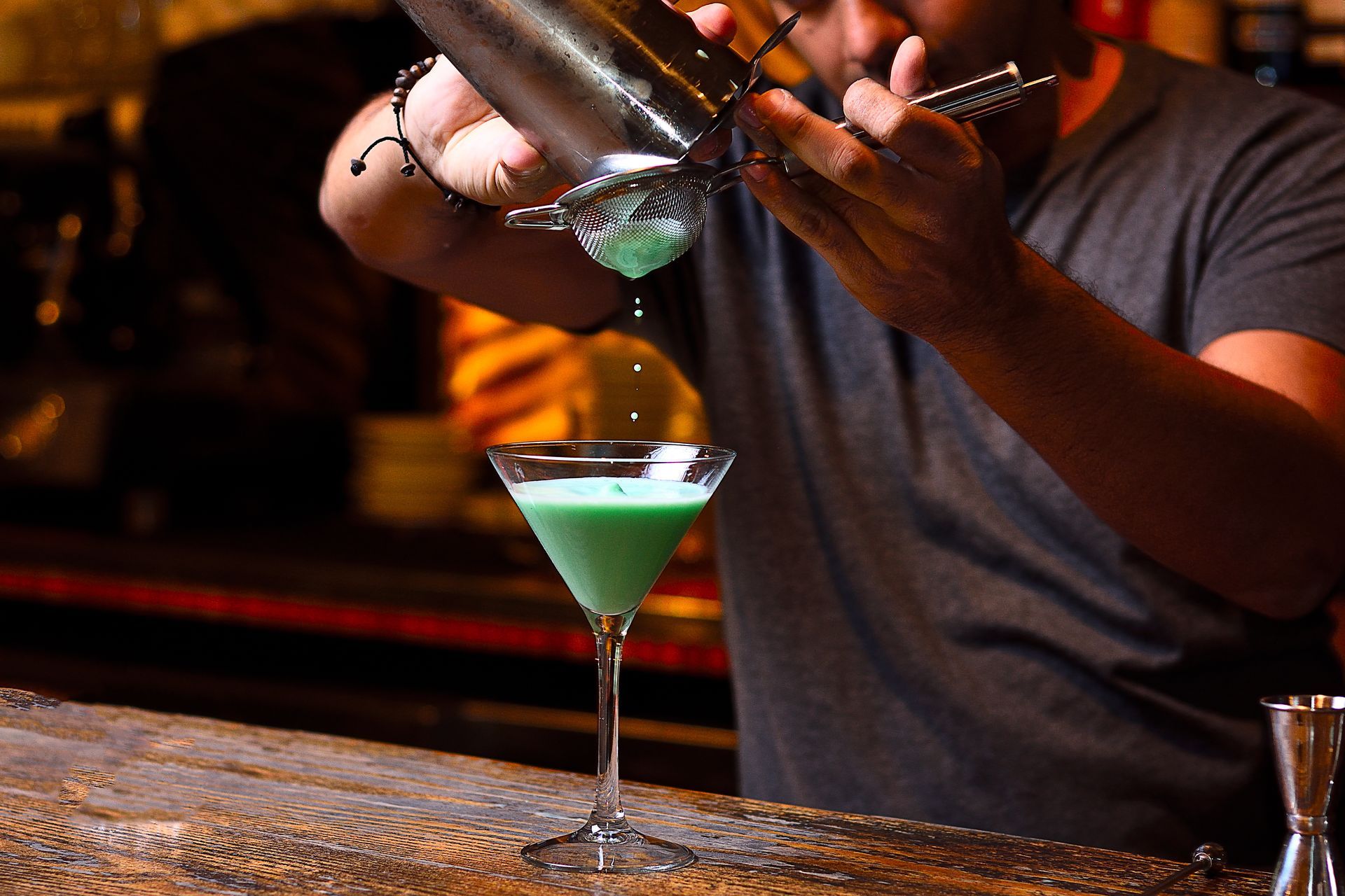A bartender is pouring green liquid into a martini glass.