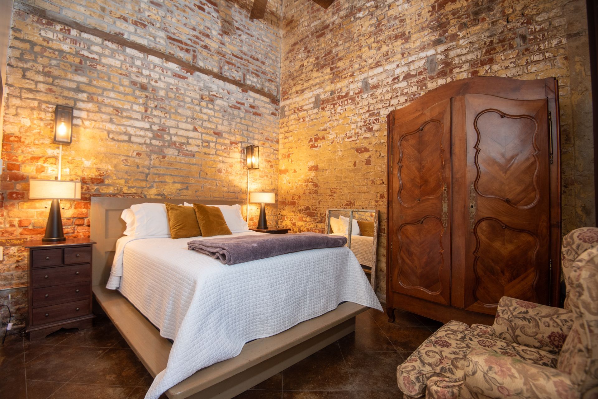 A bedroom with a brick wall , a bed , a chair and a wardrobe.