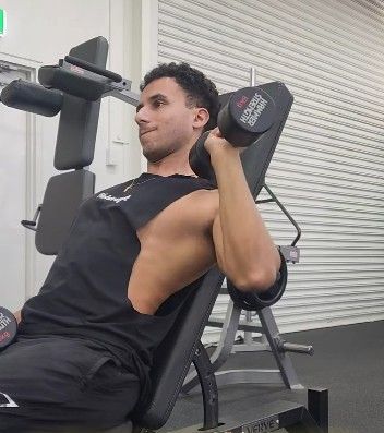 A Man is Sitting on a Bench in a Gym Holding a Dumbbell —True Form Fitness In Gwandalan, NSW