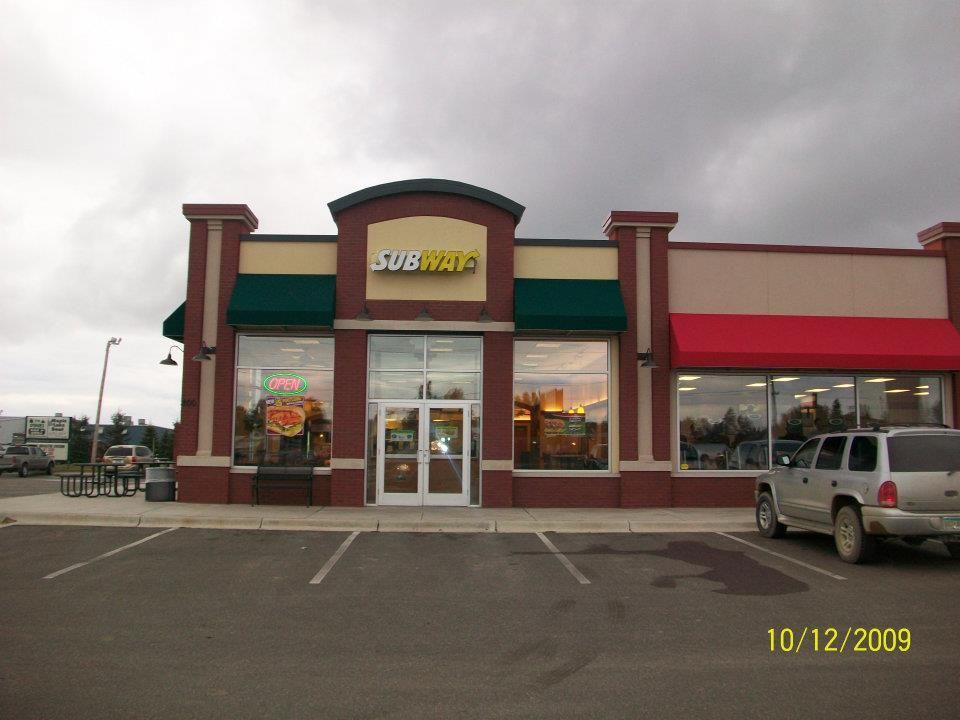 A subway restaurant with cars parked in front of it