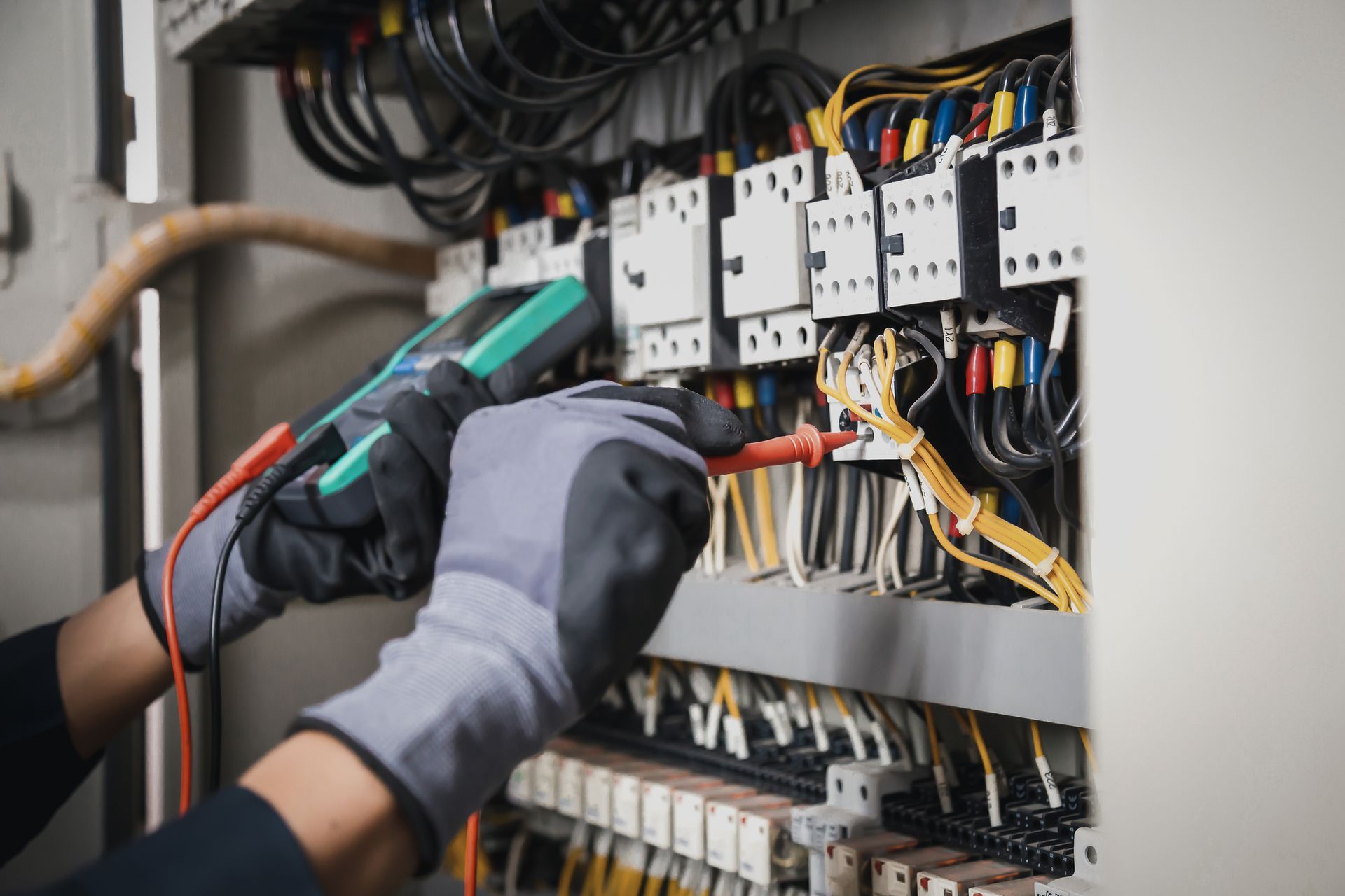 An electrician is working on an electrical panel with a multimeter.