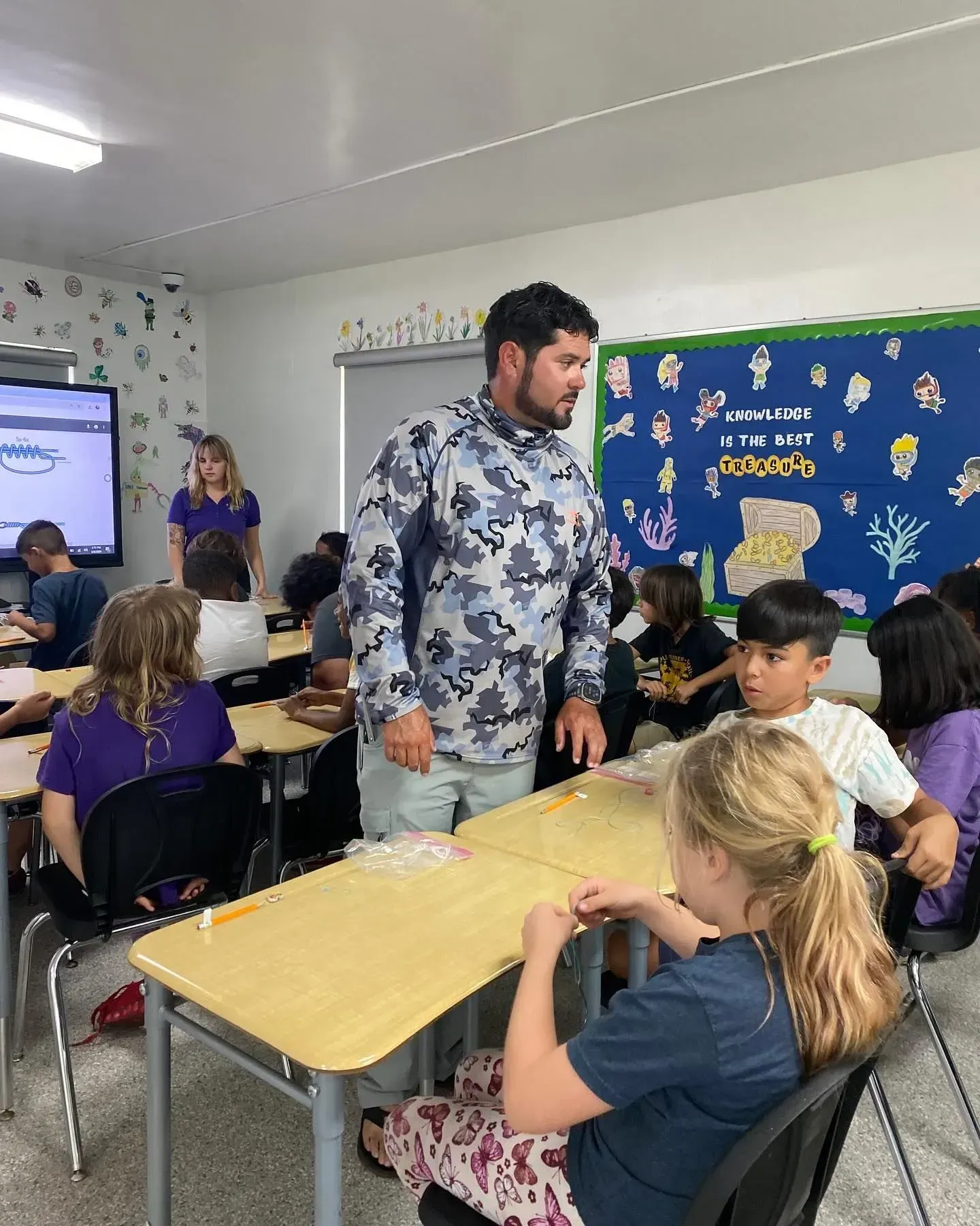 A man is standing in front of a group of children in a classroom.