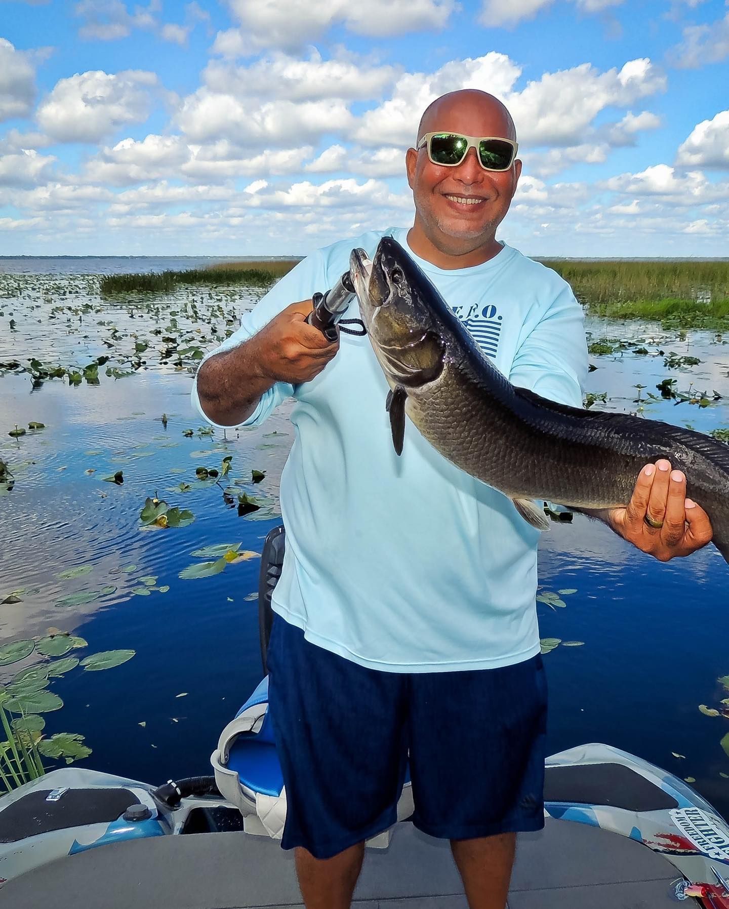 A man is holding a large fish in front of a body of water