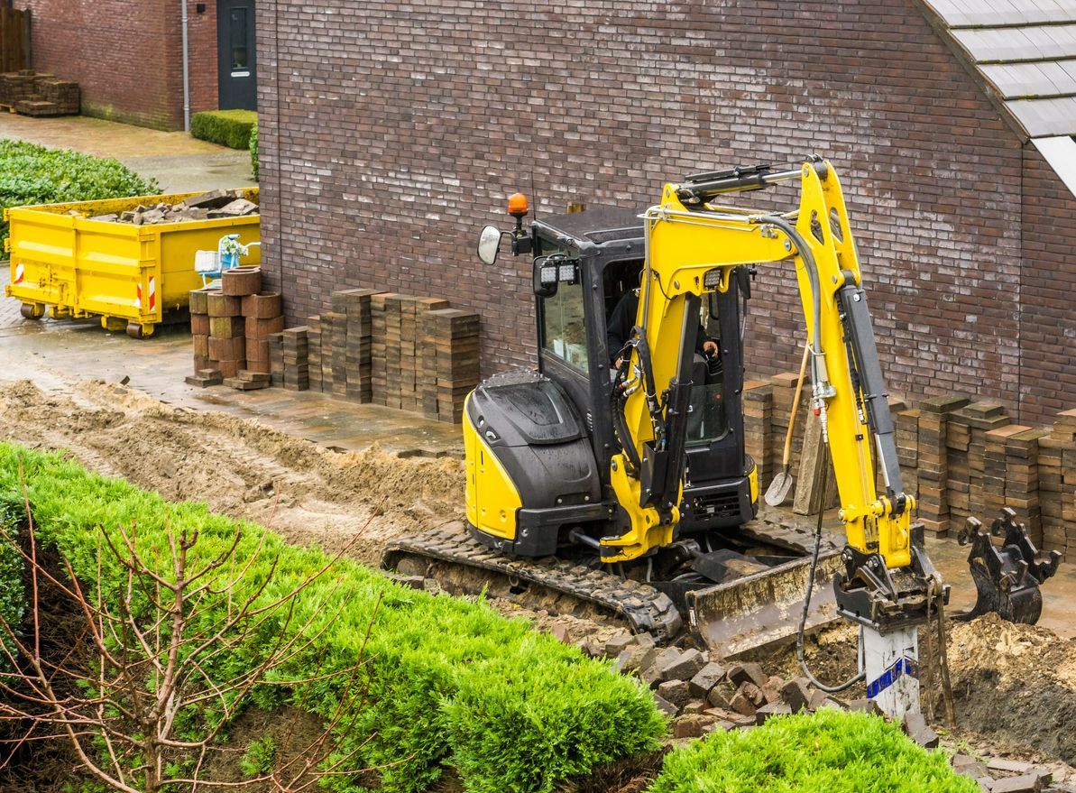 Overhead view of a construction site with an excavator digging into the earth; nearby a patch of grass and dirt road.