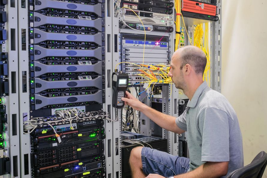 Man working on servers in a data center, using a handheld device.