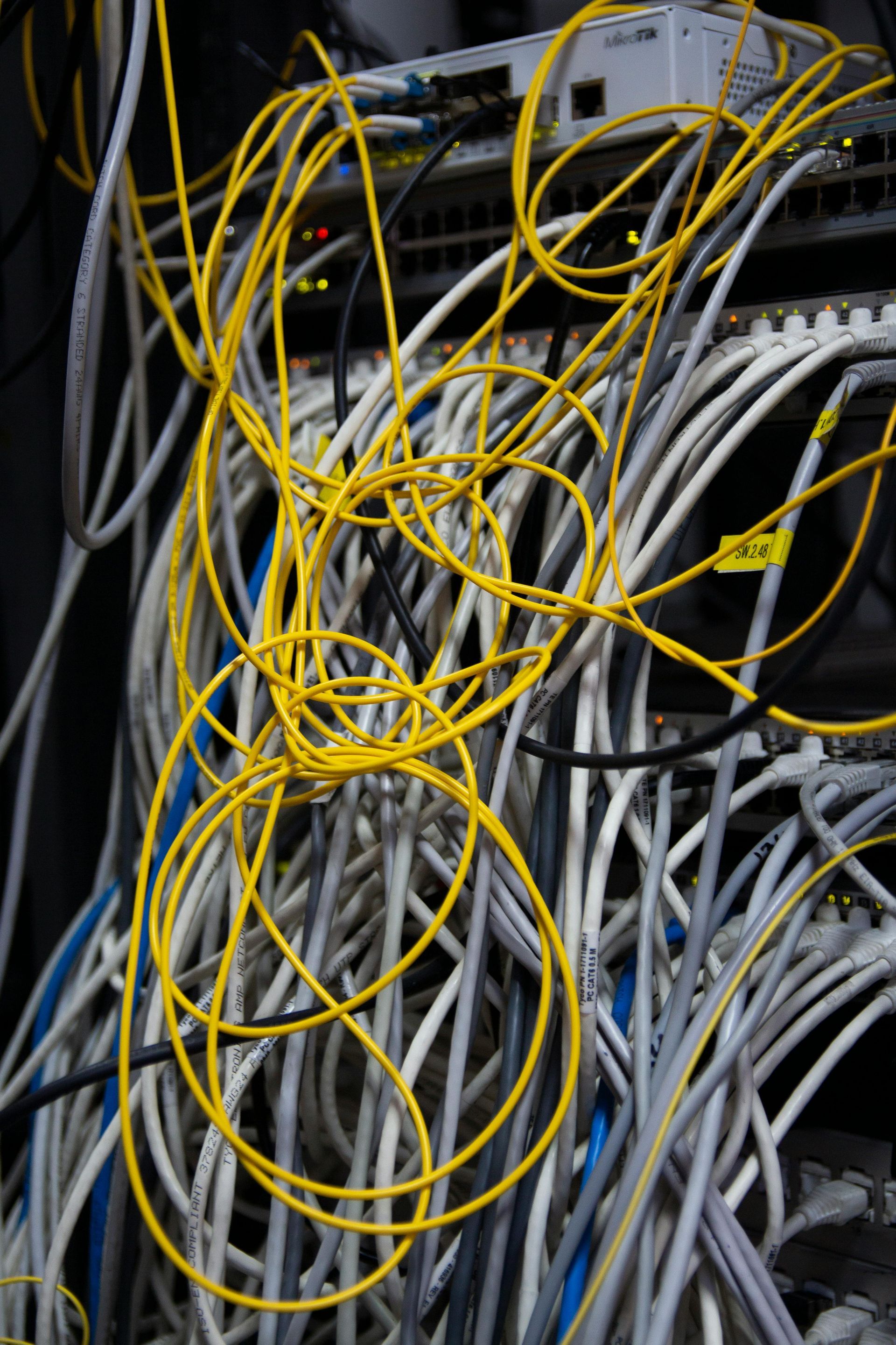Tangled network cables; many white, blue, and yellow cords in a server room.