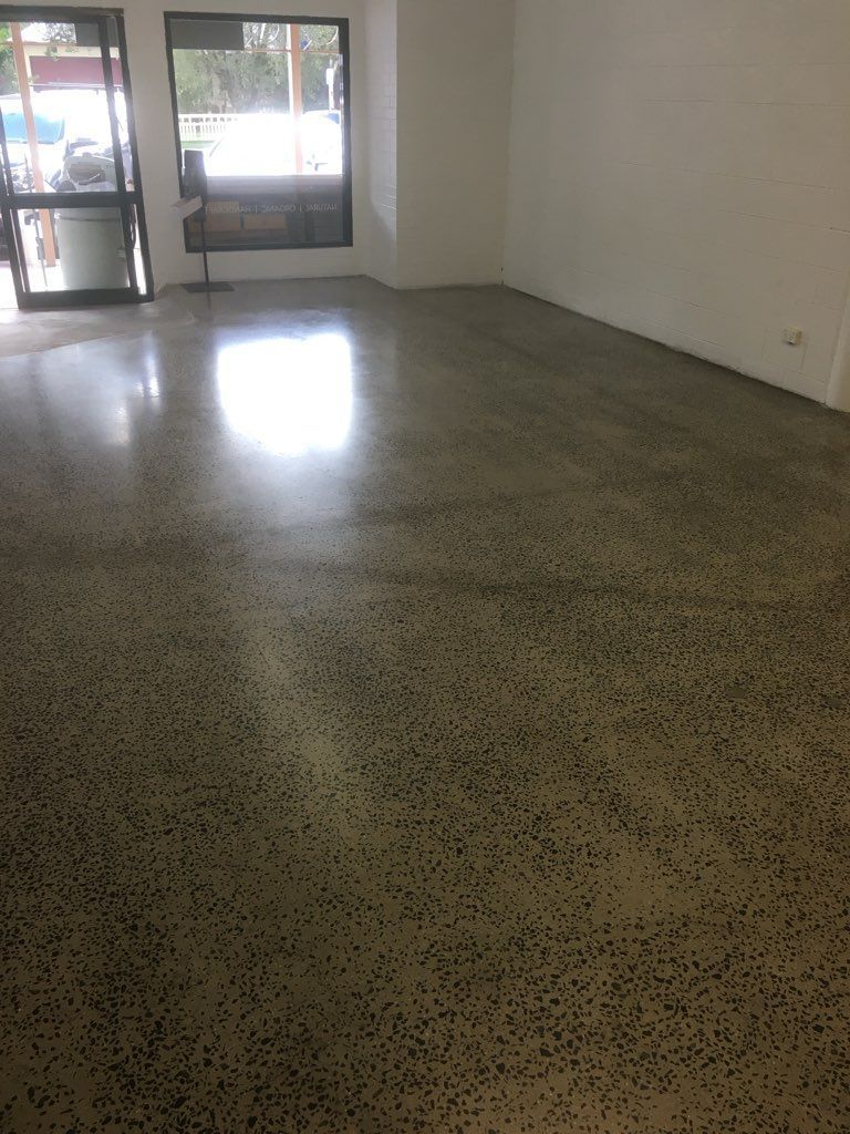 A Man Is Kneeling On The Floor While Applying Concrete — Fantastic Frank's Concrete Resurfacing In Byron Bay, NSW