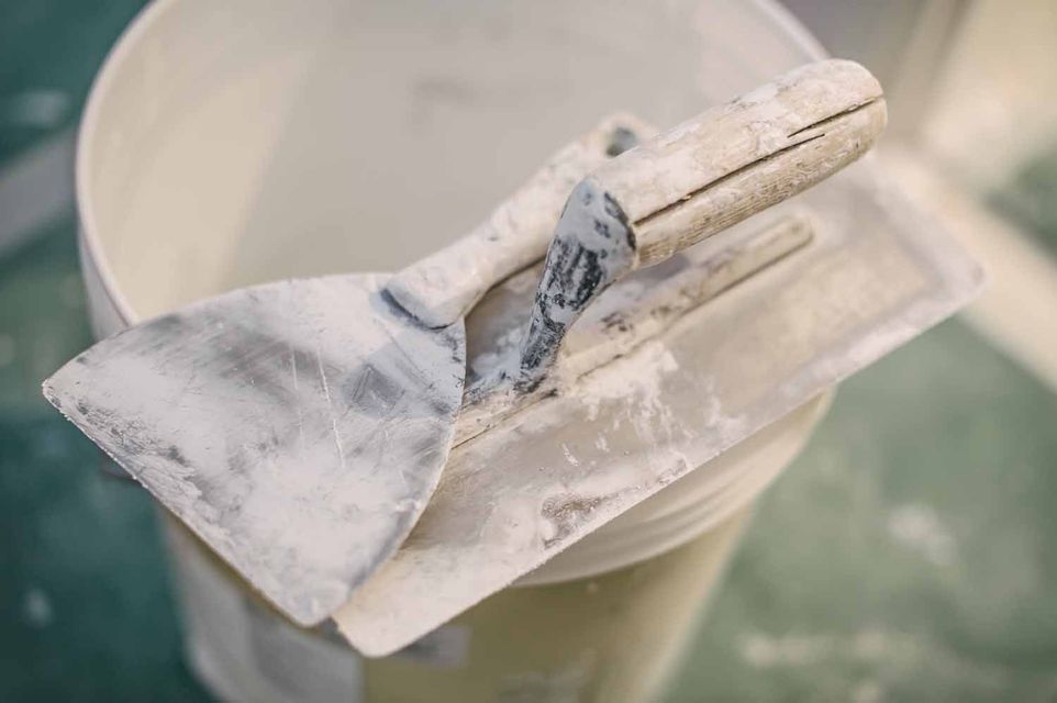 A spatula is sitting on top of a bucket of plaster.