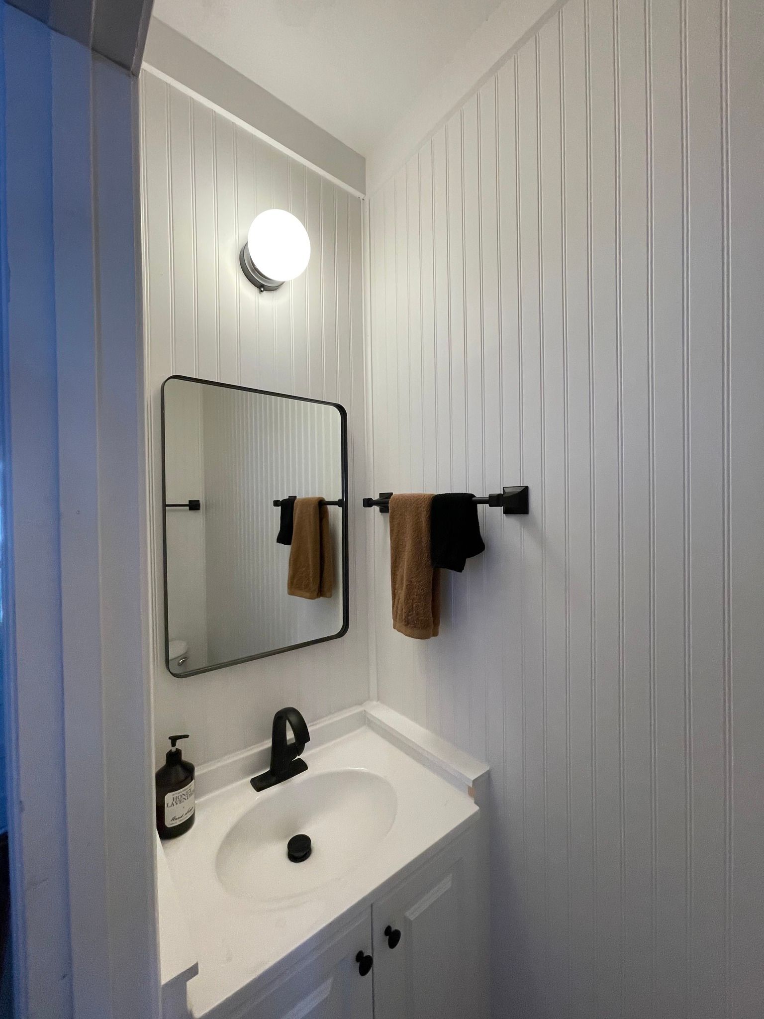 A bathroom with a sink , mirror and towels hanging on the wall.