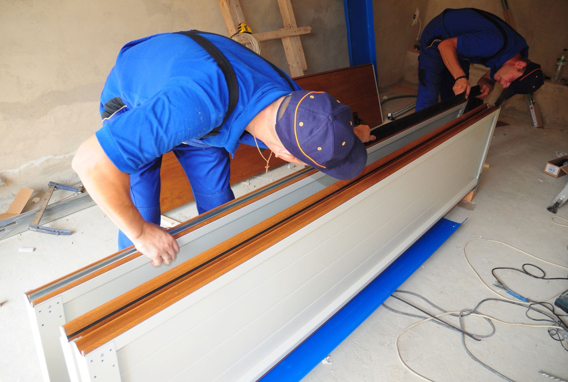 Two men in blue overalls are working on a piece of wood