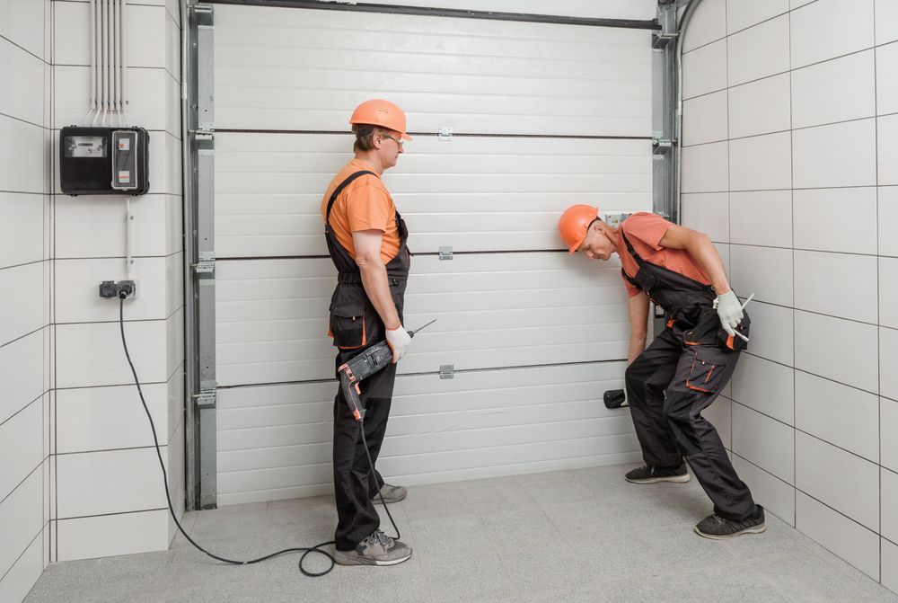 Two men are working on a garage door in a garage.