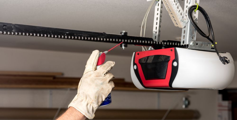 A man is kneeling down in a garage working on a garage door.