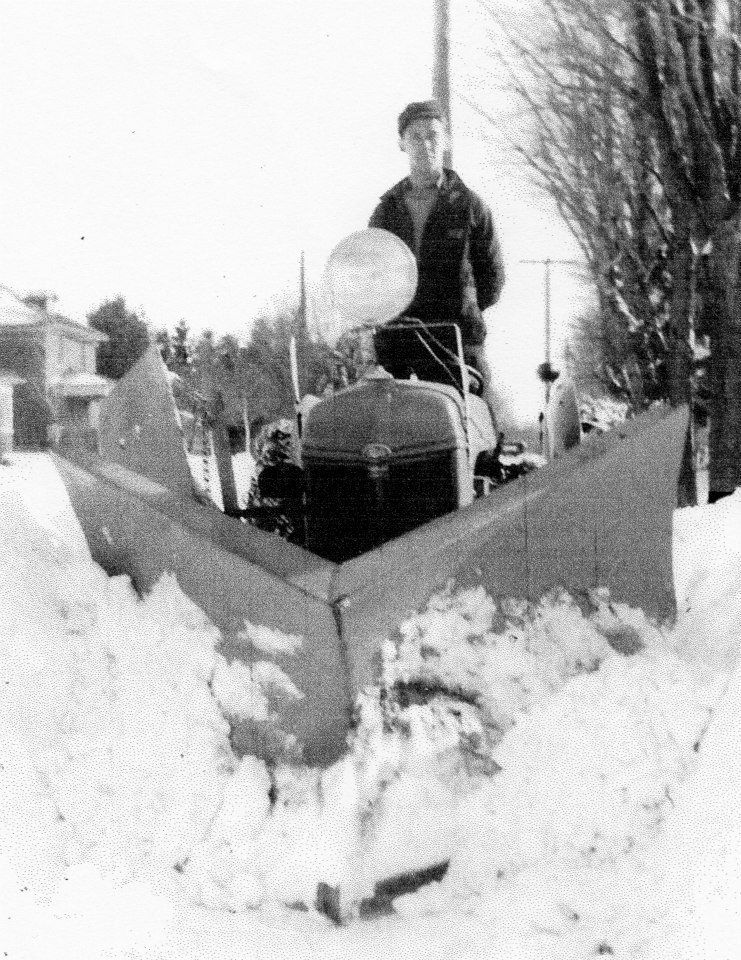 A black and white photo of a man driving a snow plow