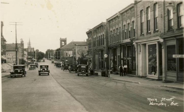 A black and white photo of a city street with cars driving down it.