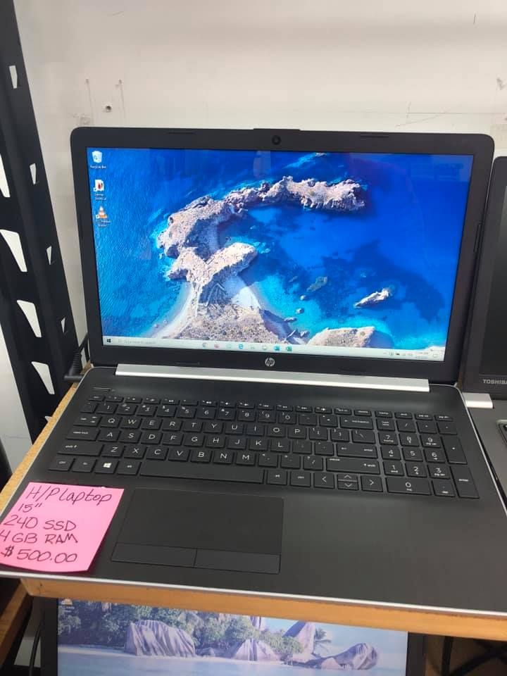 Black HP laptop on a desk with a blue ocean wallpaper and a pink sticky note on the lower left.