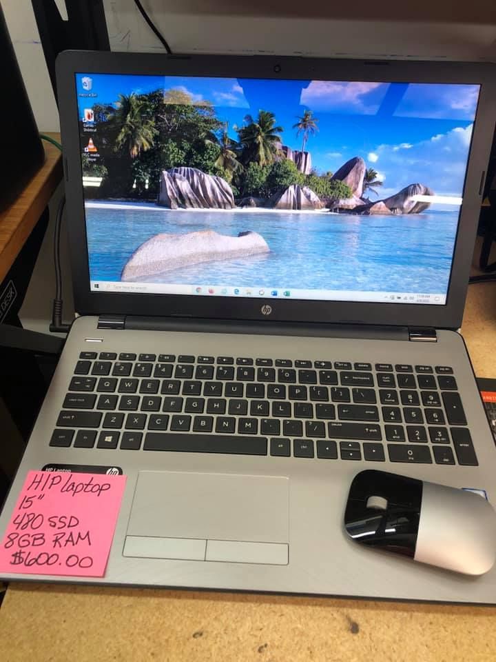 HP laptop on a desk, screen showing a tropical beach wallpaper, with a mouse and pink price note beside it