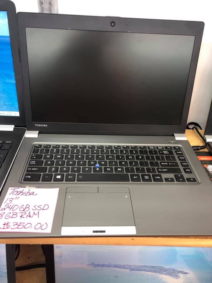Open laptop on a desk beside a handwritten sale sign and a smaller laptop edge on the left.
