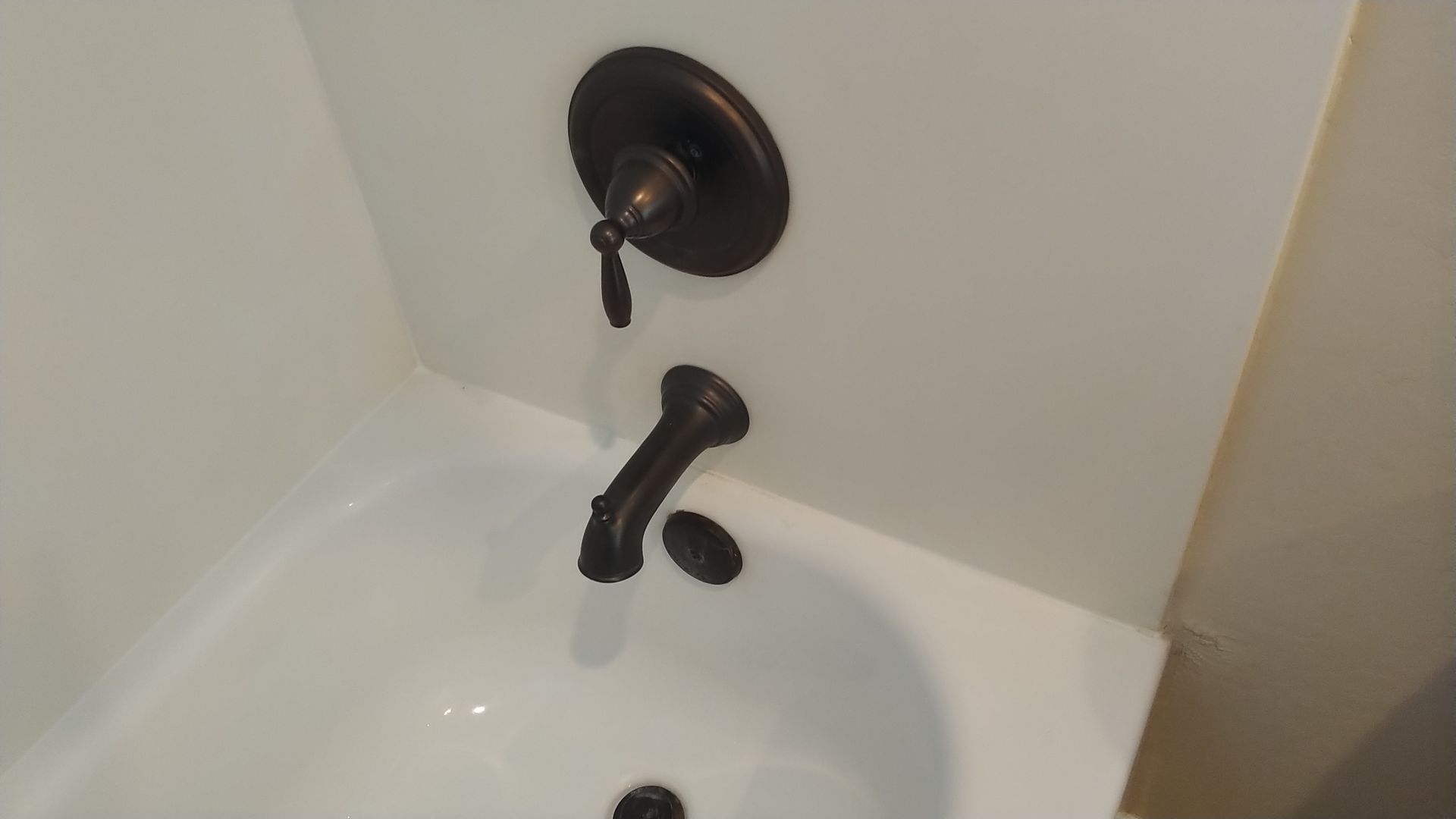 A bathtub with a brown faucet and a white wall.