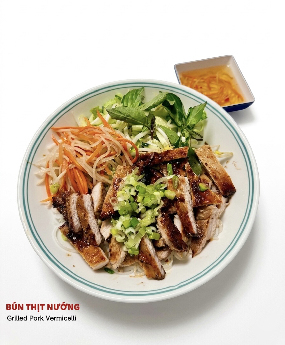 A bowl of Bun Thit Nuong with grilled pork, rice vermicelli, fresh herbs, and pickled vegetables, served with sauce.