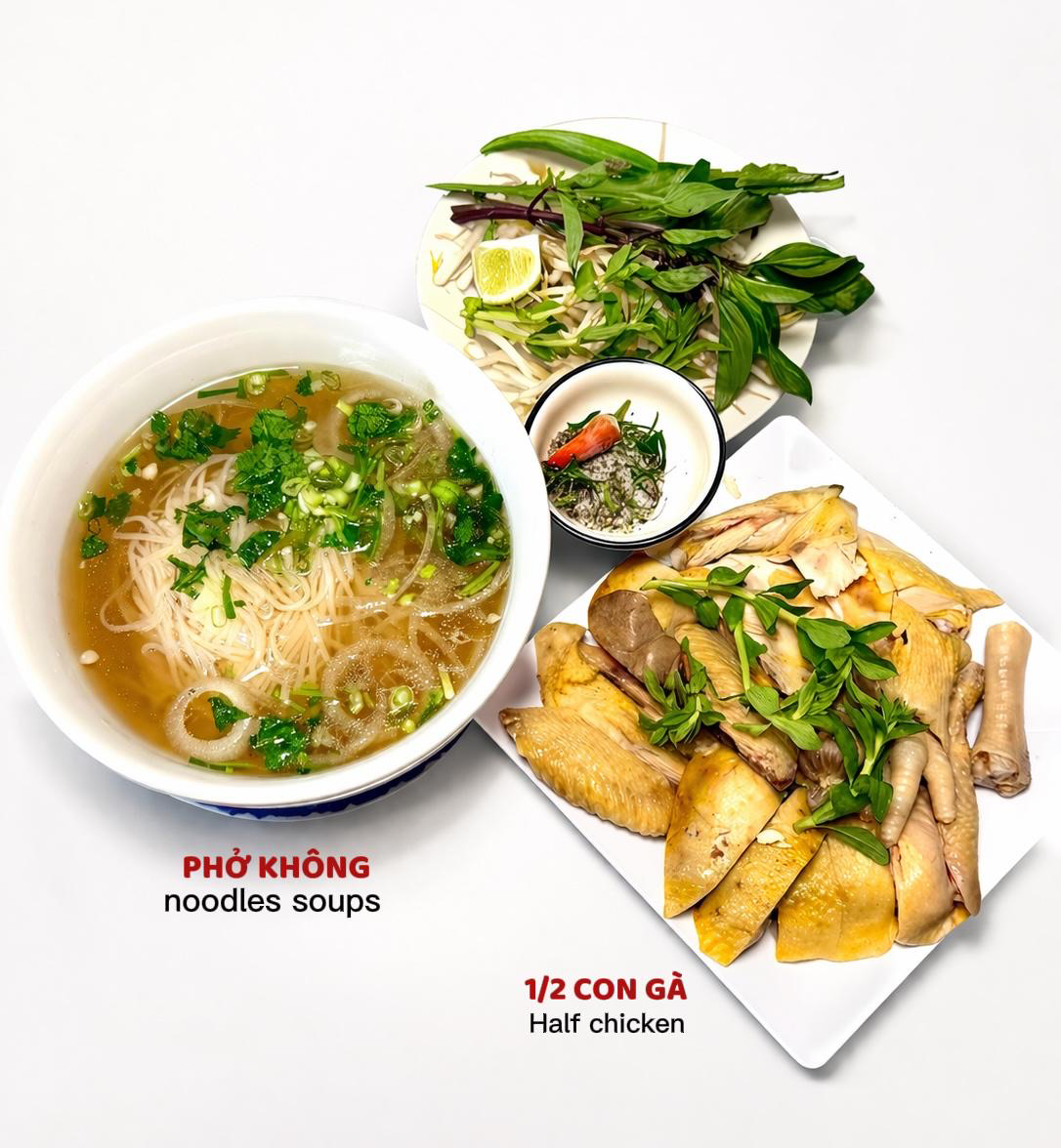 A bowl of pho soup next to a plate of chopped half chicken and a side of fresh herbs and dipping sauce.