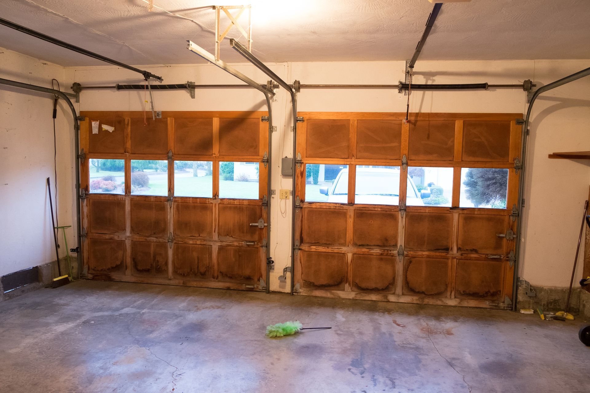 An empty garage with two garage doors open and a broom on the floor.