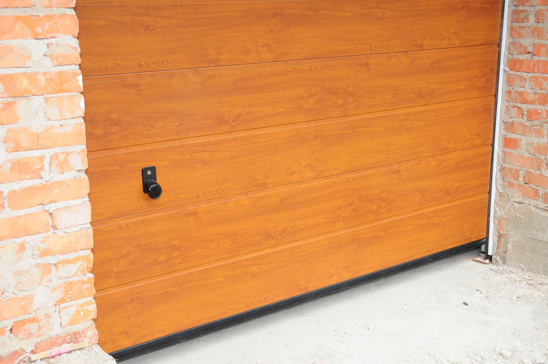 A wooden garage door is sitting next to a brick wall.