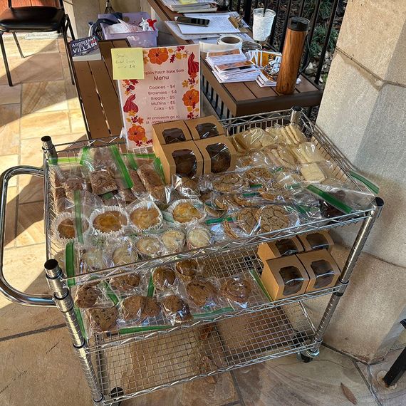 A cart filled with baked goods for sale, including cookies and brownies, with a fall-themed sign.
