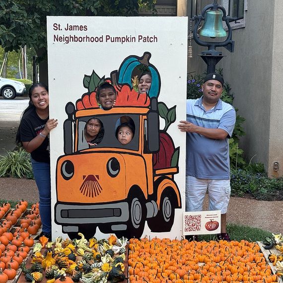 Family posing at St. James Pumpkin Patch cutout. Children peek through truck windows, smiling. Pumpkins in foreground.