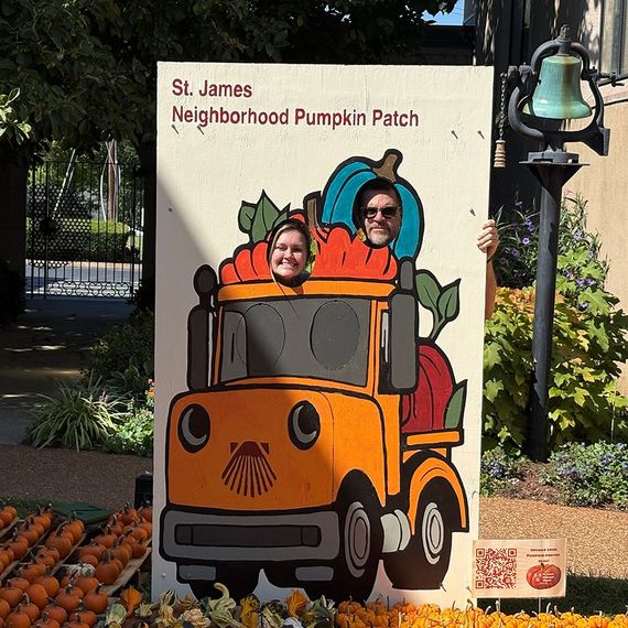Two people pose at a pumpkin patch cutout: a truck with pumpkins. St. James Neighborhood Pumpkin Patch.