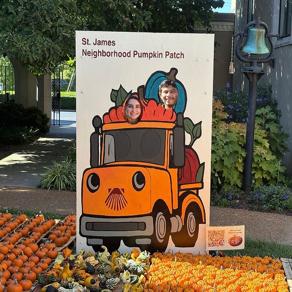 Two children with faces in a pumpkin patch cutout. Orange truck and pumpkins.