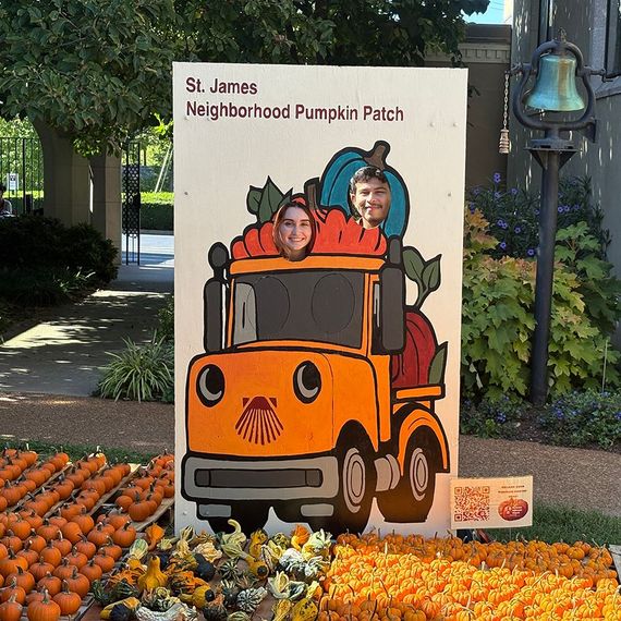 Two people with heads through a pumpkin cutout truck at a St. James pumpkin patch.