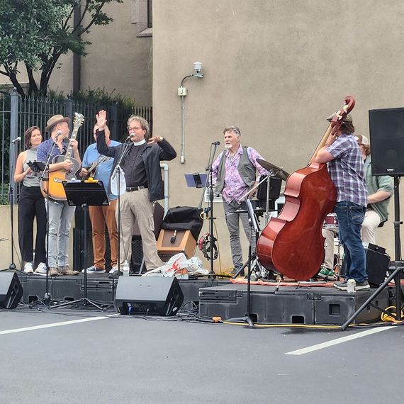 A band performs on a stage outdoors. Musicians play instruments, sing, and interact with the audience.