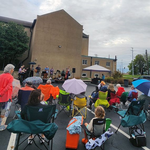 People seated in folding chairs watch a band perform outdoors under an overcast sky.