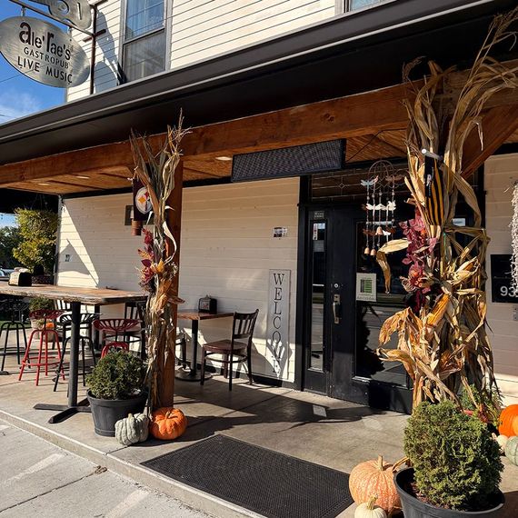 Exterior of a cafe decorated with fall foliage; outdoor seating with pumpkins and a sign reading 