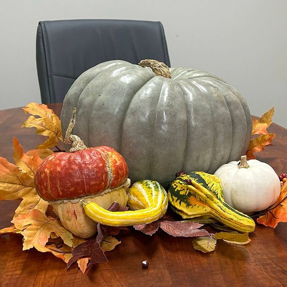 Pumpkins and gourds in autumn colors on a wooden table with fall leaves; an office setting.