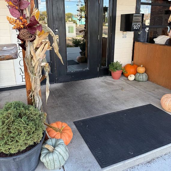 A store entrance decorated with pumpkins, corn stalks, and fall foliage. The door reads 937.