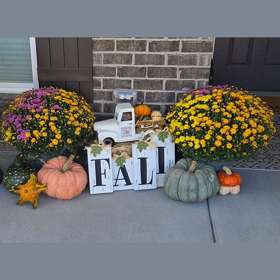 Fall porch decor with mums, pumpkins, and a decorative truck.