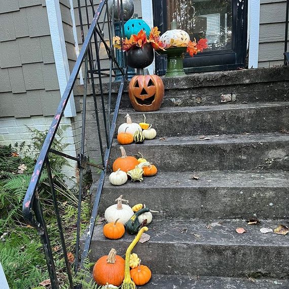 Halloween-decorated front steps: pumpkins and gourds on gray steps, jack-o'-lantern by door with fall decor.