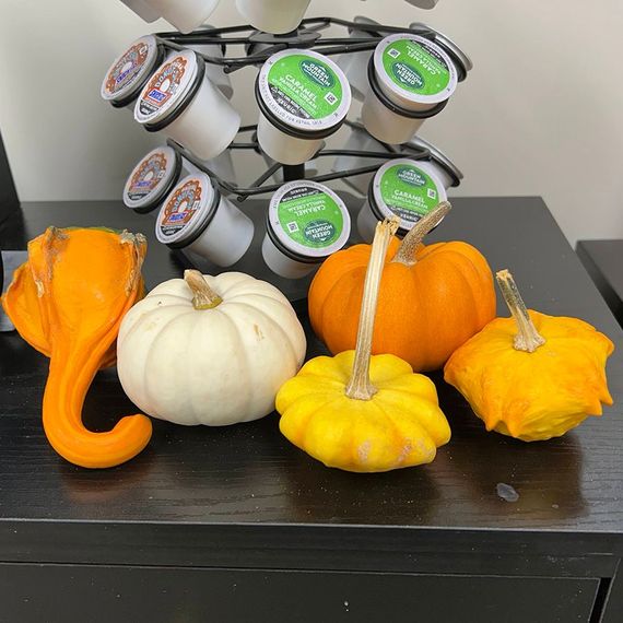 Colorful gourds on a black surface, coffee pod holder in the background.