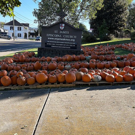 Sign for St. James Episcopal Church surrounded by pumpkins; street and buildings in the background.