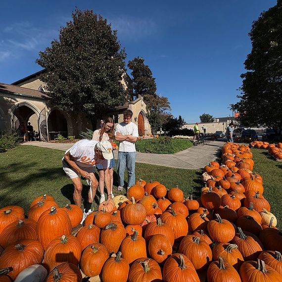People selecting pumpkins at a pumpkin patch in front of a church on a sunny day.
